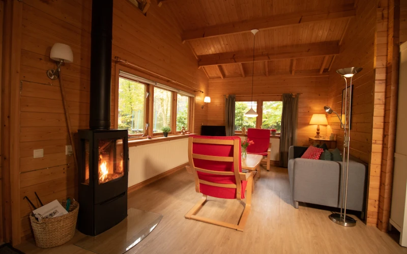 Woonkamer van Het Houten huis – sfeervolle zithoek met houten bungalow, houtkachel, privacy, met uitzicht op het groen.