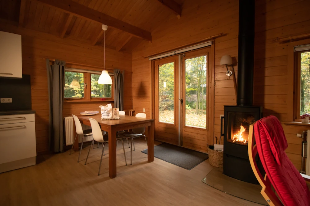 Woonkamer van Het Houten huis – sfeervolle zithoek met houten bungalow, houtkachel, privacy, met uitzicht op het groen.